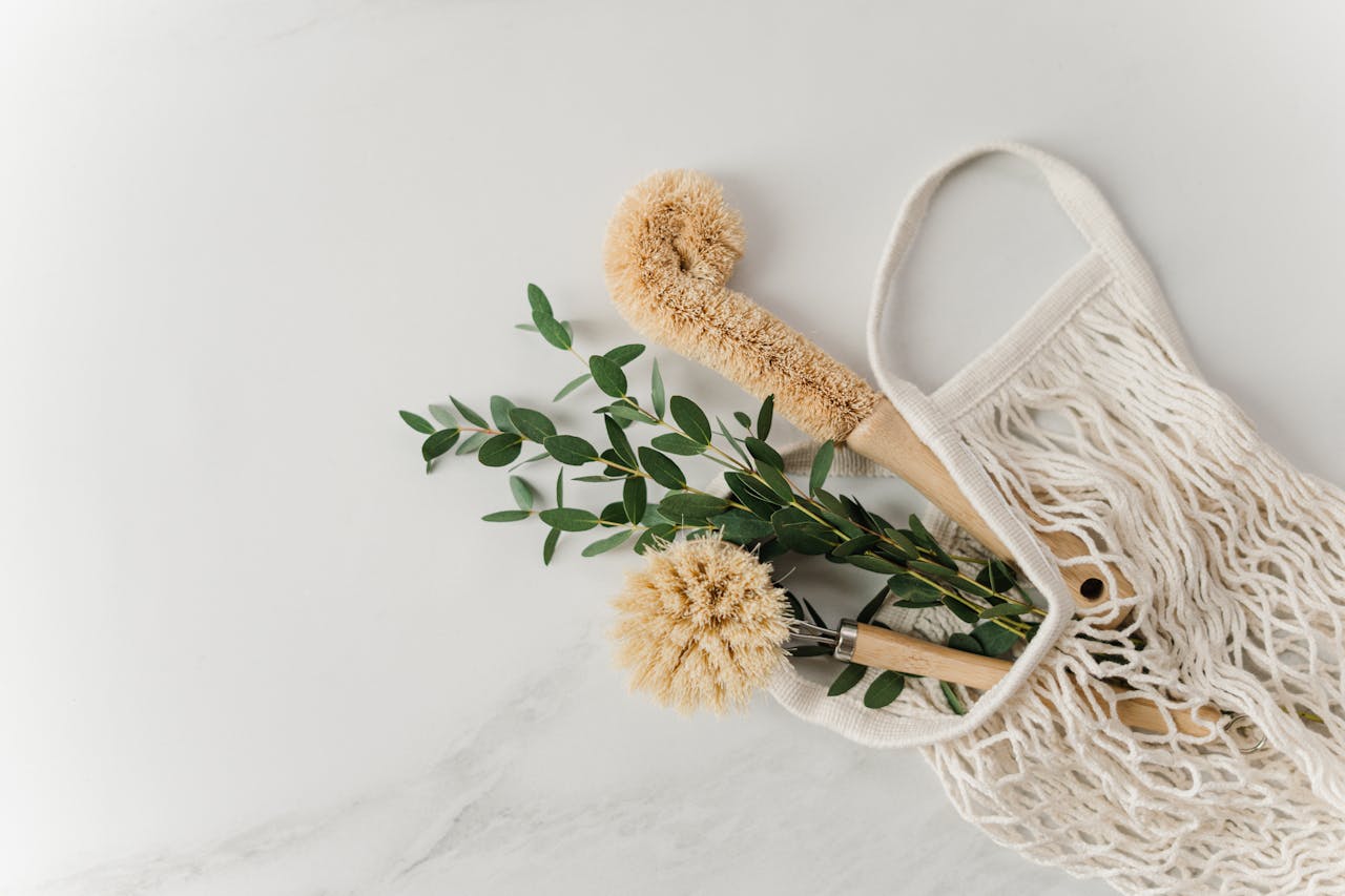 why-choose-us-03 Eco-friendly cleaning brushes and eucalyptus branches in a reusable net bag on white surface.