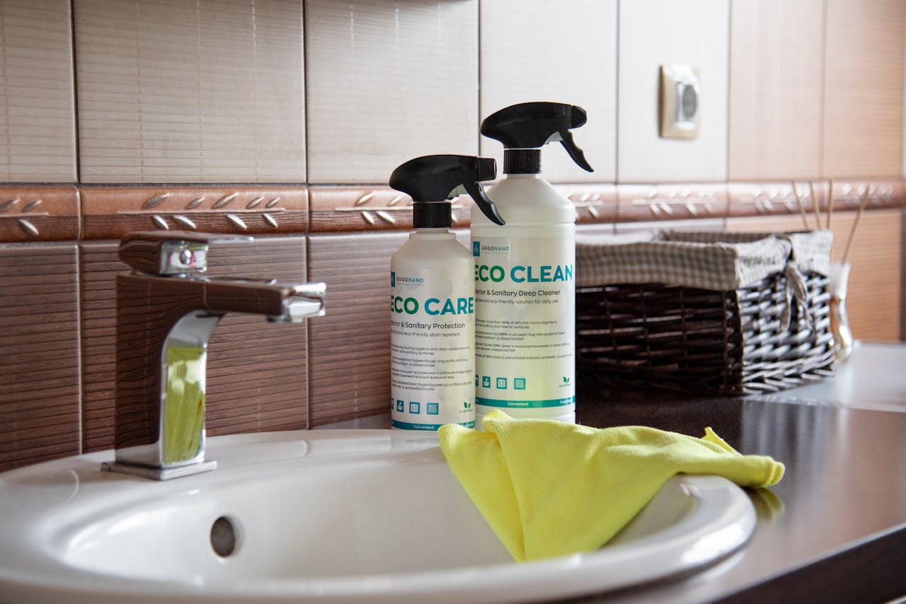 hero-02 Eco-friendly cleaning products displayed on a bathroom sink with tiles and a basket.